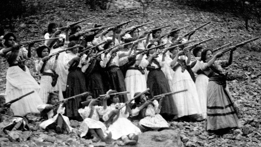 Một nhóm gồm nhiều phụ nữ và các bé gái mặc trang phục truyền thống cùng luyện tập kỹ năng bắn ...