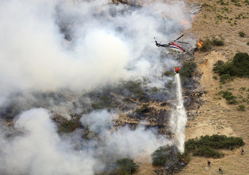 Các nhân viên cứu hỏa chiến đấu với đám cháy rừng từ mặt đất khi một chiếc trực thăng thả nước lên trên ở Springville, bang Utah, Mỹ vào thứ Hai, ngày 1 tháng 8 năm 2022. Đám cháy bắt đầu khi một người đàn ông cố gắng đốt một con nhện bằng bật lửa.