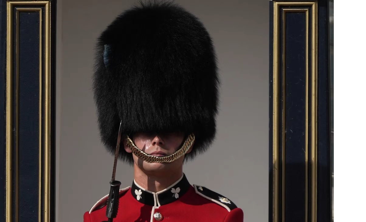 Một người lính Anh đội chiếc mũ da gấu truyền thống đổ mồ hôi bên ngoài Cung điện Buckingham ở ...